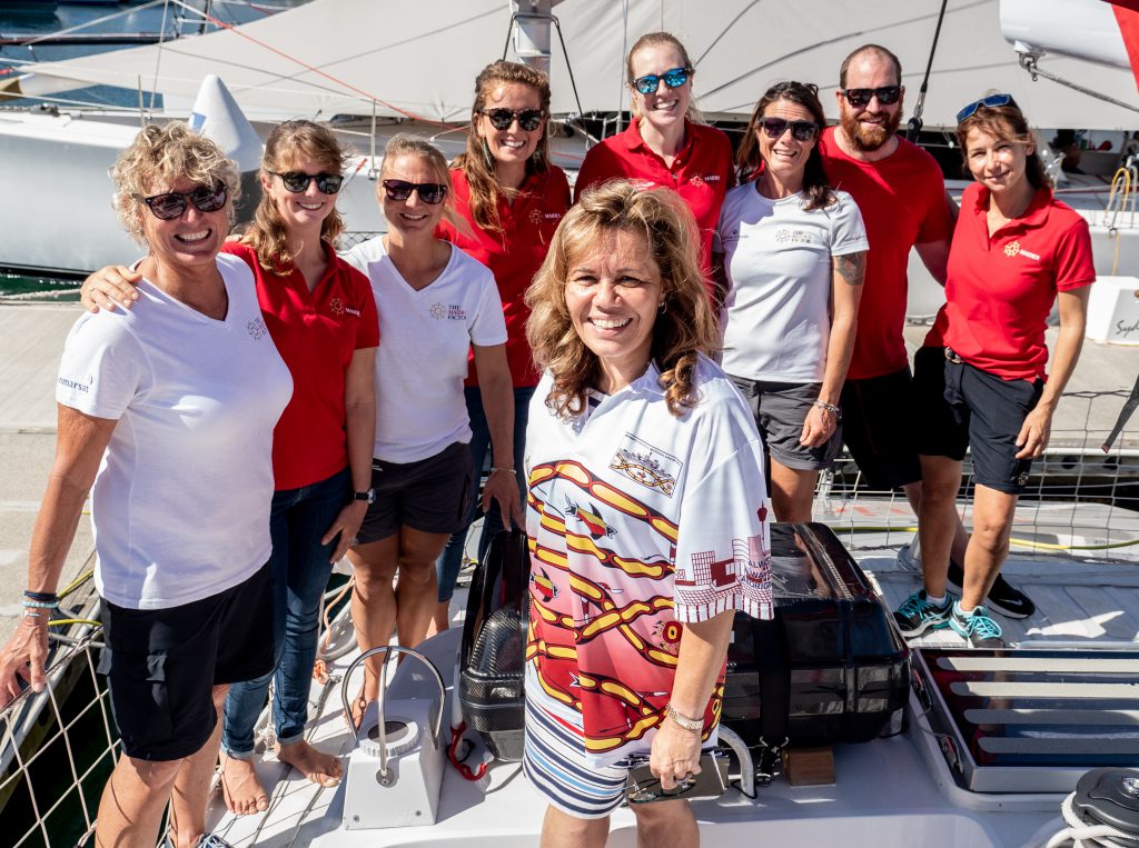 Yvonne Weldon stands centre frame. Behind her, all also standing on the boat, are the Maiden crew. Wendy Tuck is on the far left.