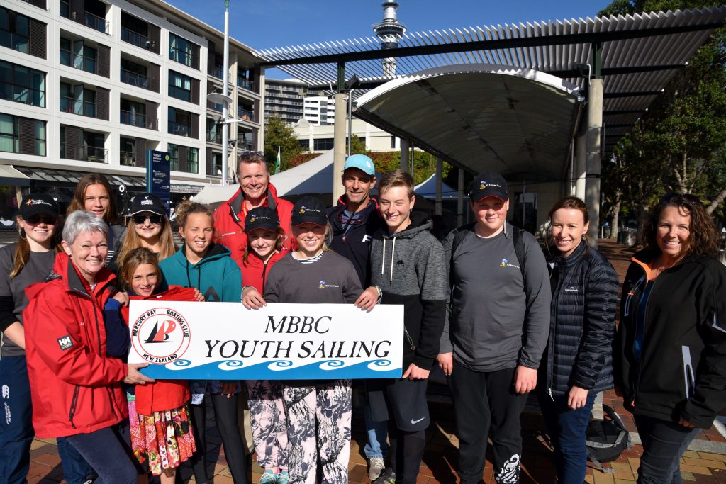 Students stand with Tracy Edwards and Greg Bint from TMF team holding a sign that says "MBBC Youth Sailing"