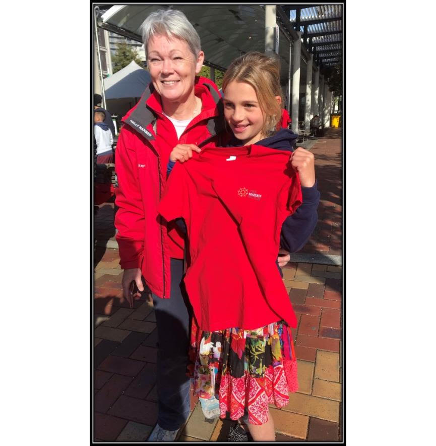 Tracy Edwards stands next to a young girl. Tracy is wearing a red jacket and fleece. The girl is holding up a red t-shirt 