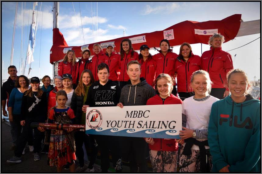MBBC young people stand in front of Maiden, holding an MBBC sign. The crew stand behind in red jackets on Maiden