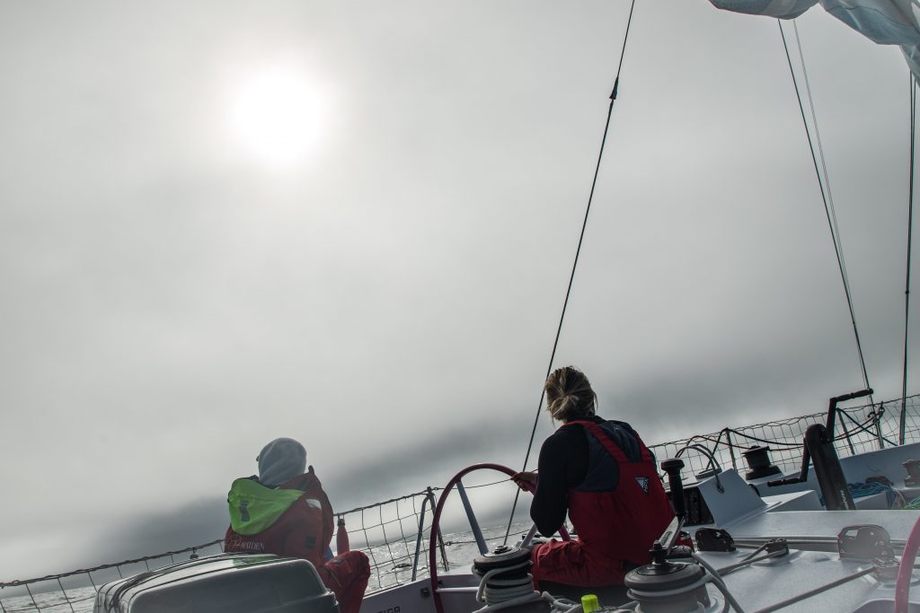 A grey foggy morning with the sun behind the clouds. Two crew members are on deck