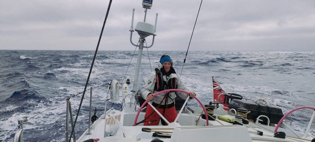 Skipper Sharon at the helm, a dark and gloomy sea behind her with small waves